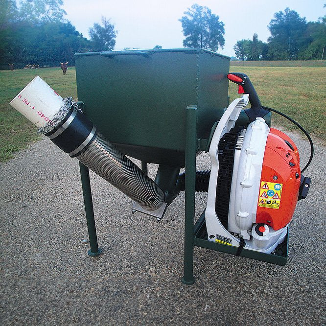 A green wildlife feeder with an attached orange air-driven feed system, placed in an outdoor setting.