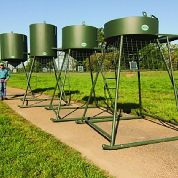 A series of green metal corn feeders mounted on stands, designed for use in fields.