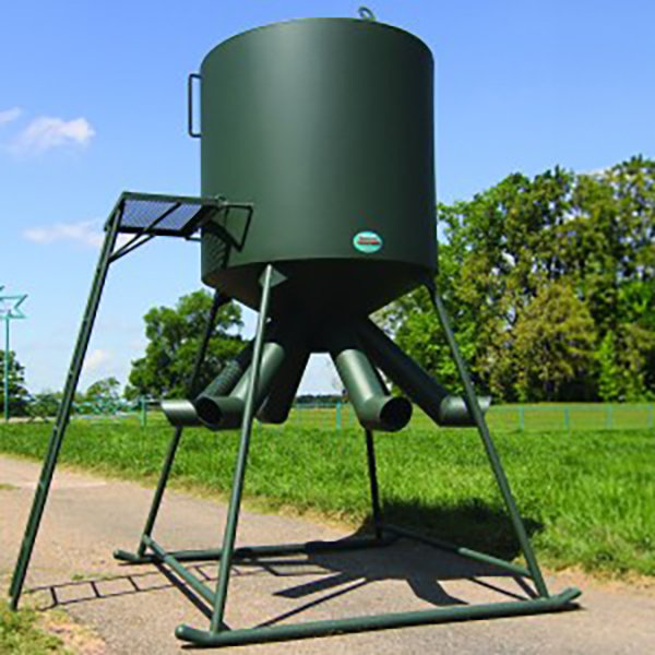 A green CP 6-Tube Protein Feeder mounted on a metal stand, positioned outdoors on a sunny day.
