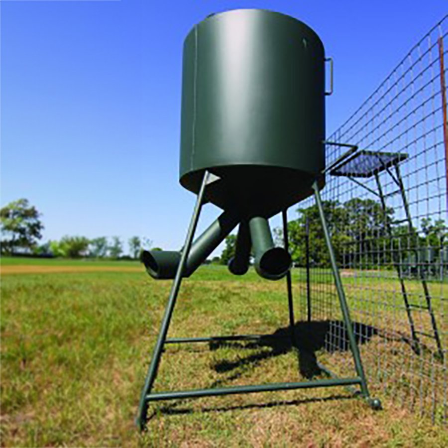 A green CP Breeding Pen Feeder positioned alongside a metal fence in an outdoor setting.