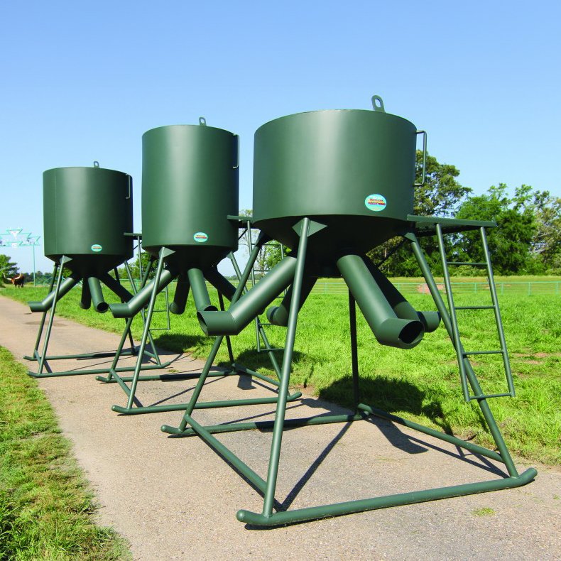 A series of green protein feeders for animals, mounted on metal stands, designed for gravity flow feeding.
