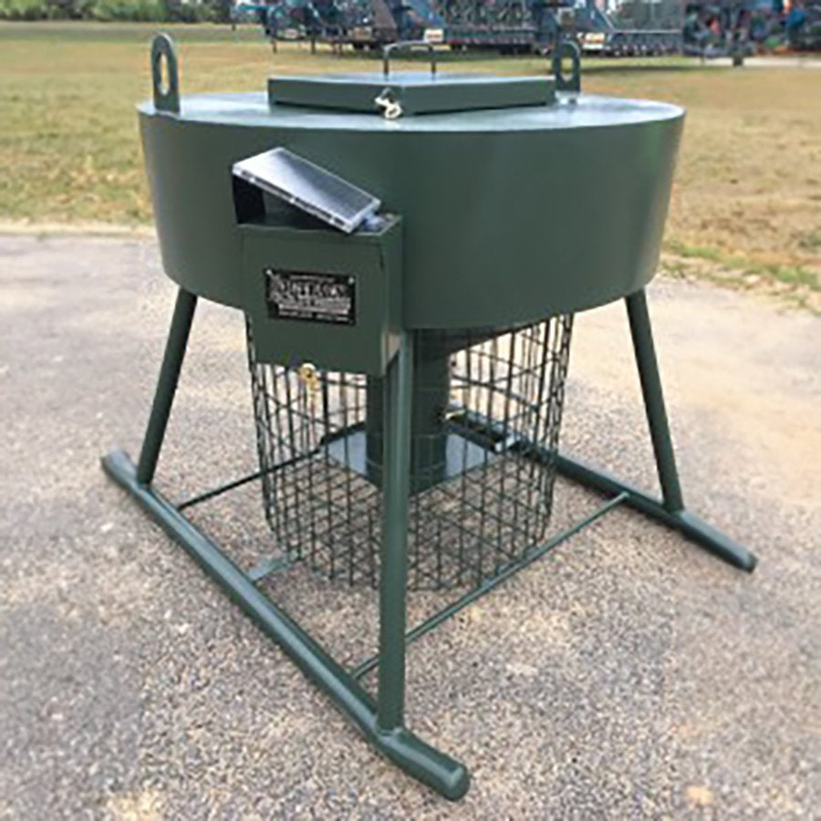 A green metal regulated turkey feeder with a metal frame and a label on the side, placed on a concrete surface.