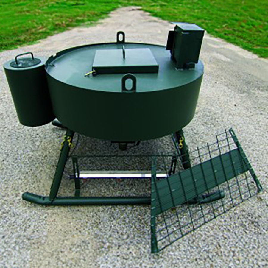 A green wildlife feeder and water station on a ground surface, equipped with a metal grid and a water reservoir.