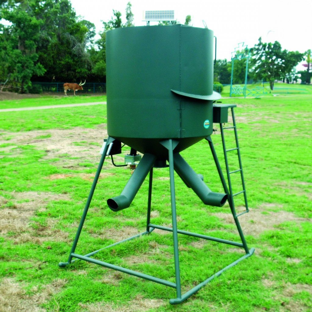 A green wildlife feeder with a metal structure, placed on a grassy field.