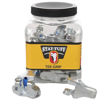 A clear plastic container with a black lid labeled 'STAY-TUFF' containing silver Tee-Grips, with some Tee-Grips scattered outside the container.